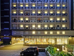 Ein modernes Gebäude mit einheitlicher Fassade, zahlreichen Fenstern und einem gut sichtbaren Eingang, vor dem ein Auto geparkt ist.