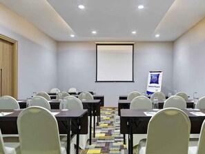 A conference room with tables, chairs, a projector screen, and a banner. - Hotel ibis budget Jakarta Airport (Tangerang)