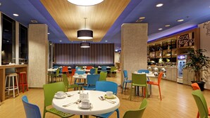 A modern restaurant with round tables, colorful chairs, and a bar area. - Hotel ibis budget Jakarta Airport (Tangerang)