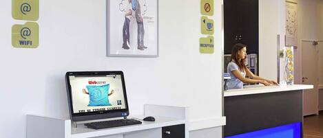 A reception desk with a laptop displaying a website, a framed picture above the desk, and directional signs on the wall.