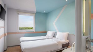 Una habitación de hotel con dos camas, un ventanal con vistas, un baño con lavamanos y espejo, y un televisor de pantalla plana en la pared.