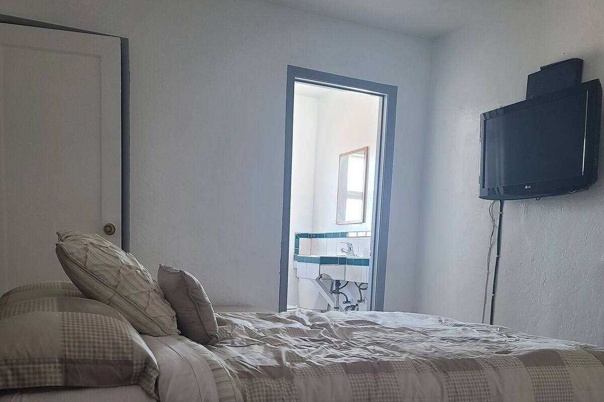 A bedroom with a bed, pillows, a television mounted on the wall, and a door leading to a bathroom.