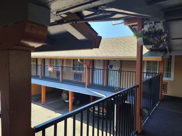 A building with a covered outdoor area, a balcony with a railing, and hanging flower baskets.