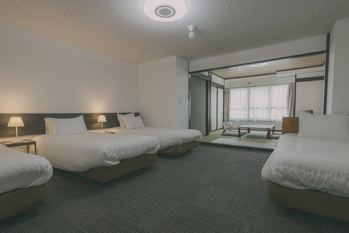 A hotel room with three beds, a large window with curtains, a sofa, and a small table.