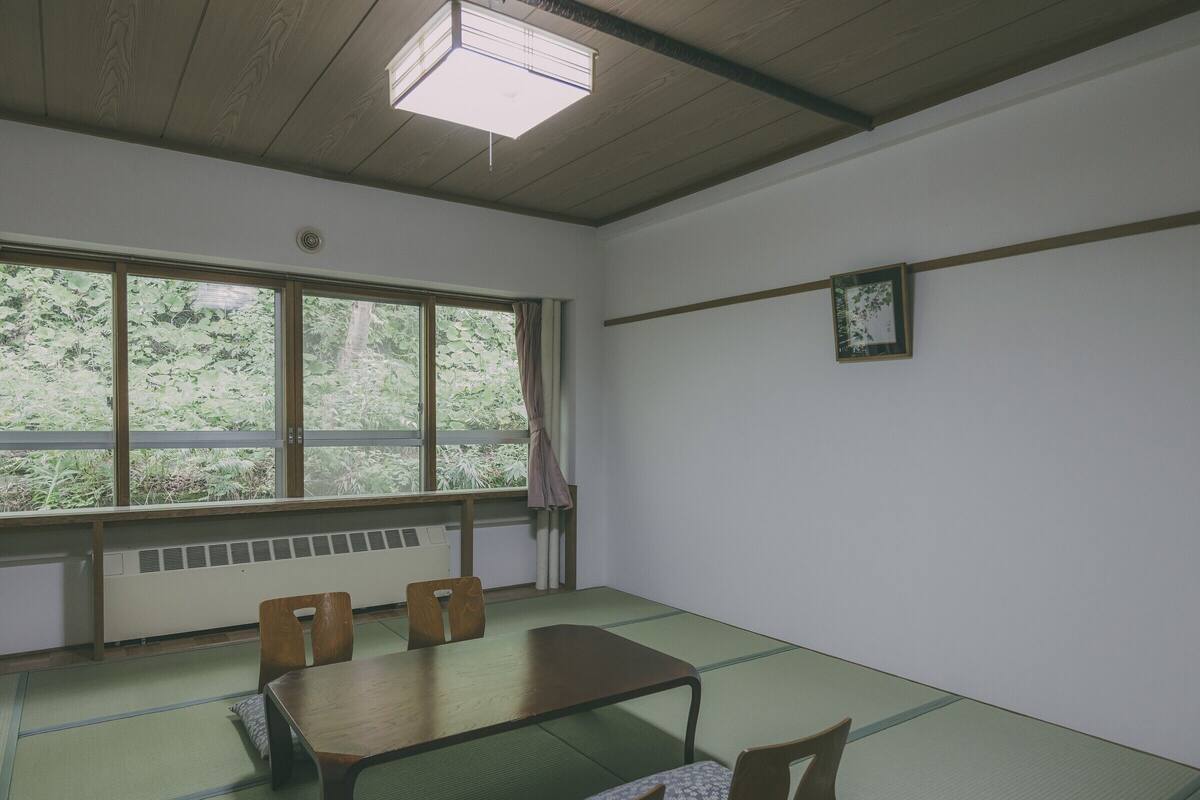 A room with tatami mats, a low table, and four wooden chairs.
