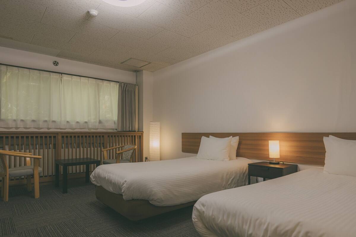 A hotel room with two beds, a desk, a chair, and a window with curtains.