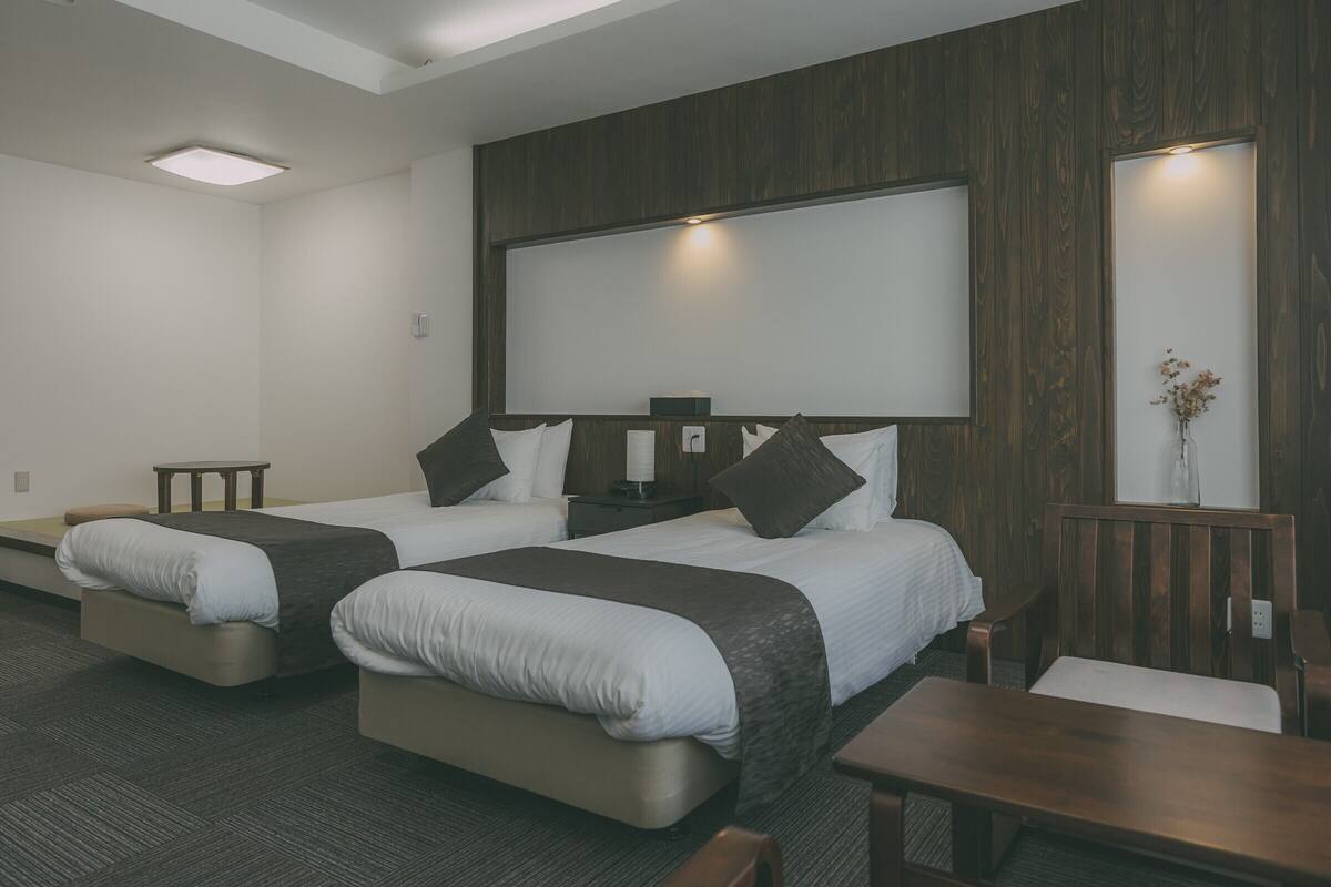 A hotel room with two beds, a large mirror, a small table, and a vase with flowers.