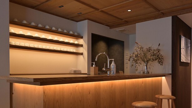 Een houten bar met een aanrecht, een spoelbak en drie barkrukken.