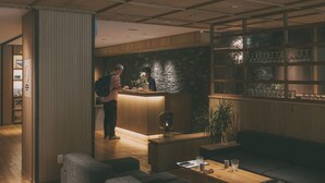 Een moderne receptie met een houten balie, een stenen muur en een zithoek met een bank en een tafel.