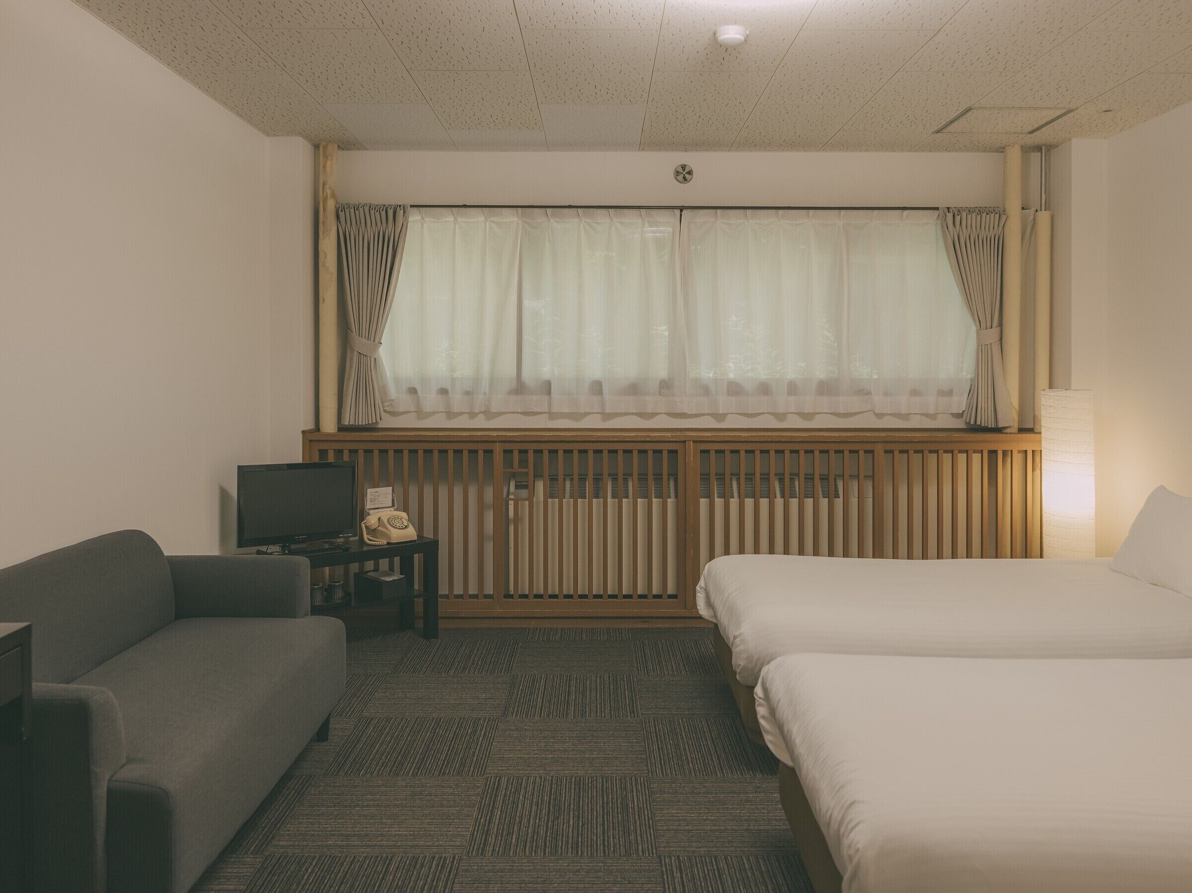 Una habitación de hotel con cama, sofá, escritorio y teléfono, y un televisor.