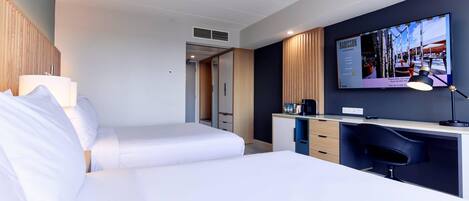 A hotel room with two beds, a desk with a chair, a TV mounted on the wall, and a wardrobe.