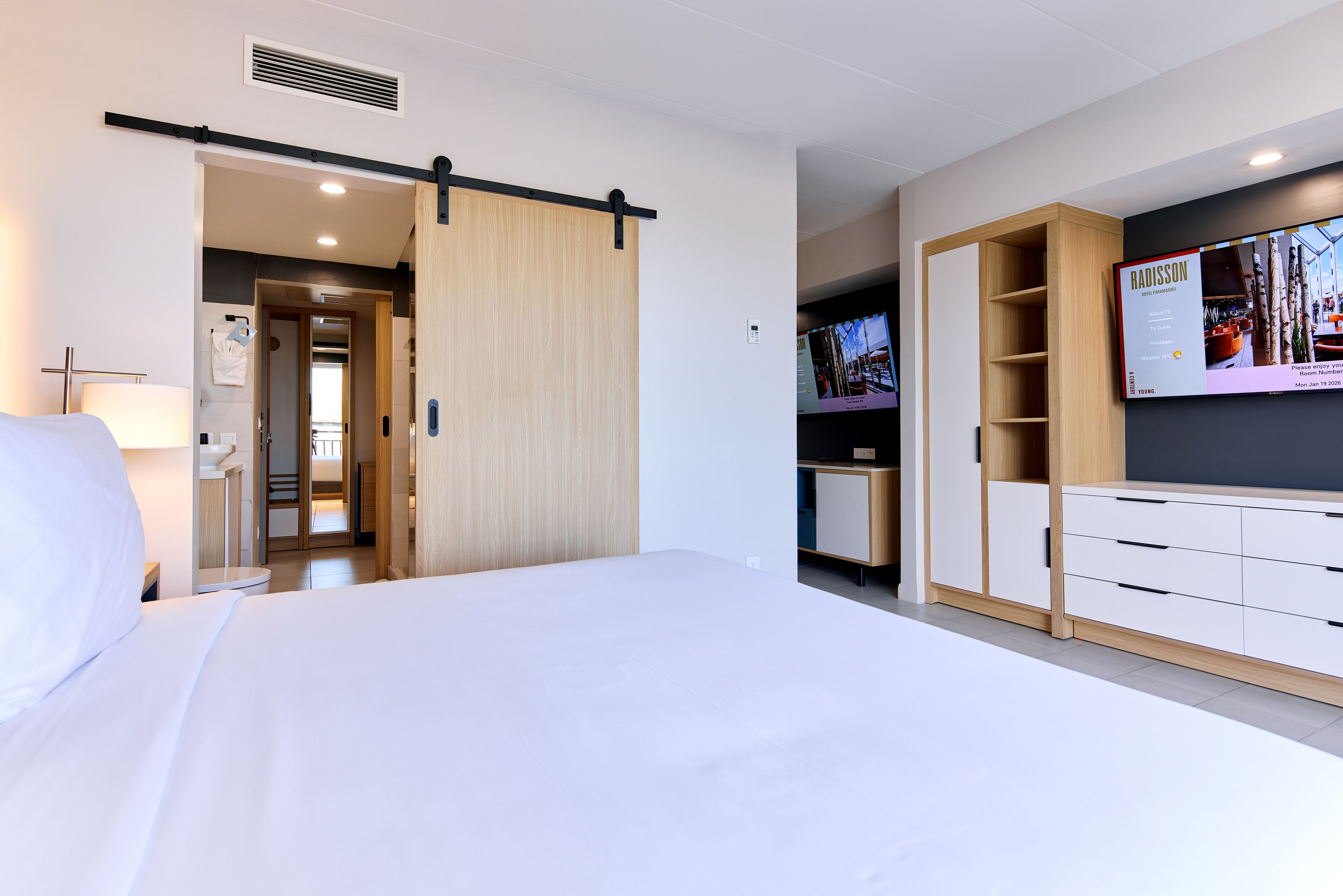 Une chambre d’hôtel moderne avec un grand lit, un placard à portes coulissantes, une télévision et une armoire en bois.