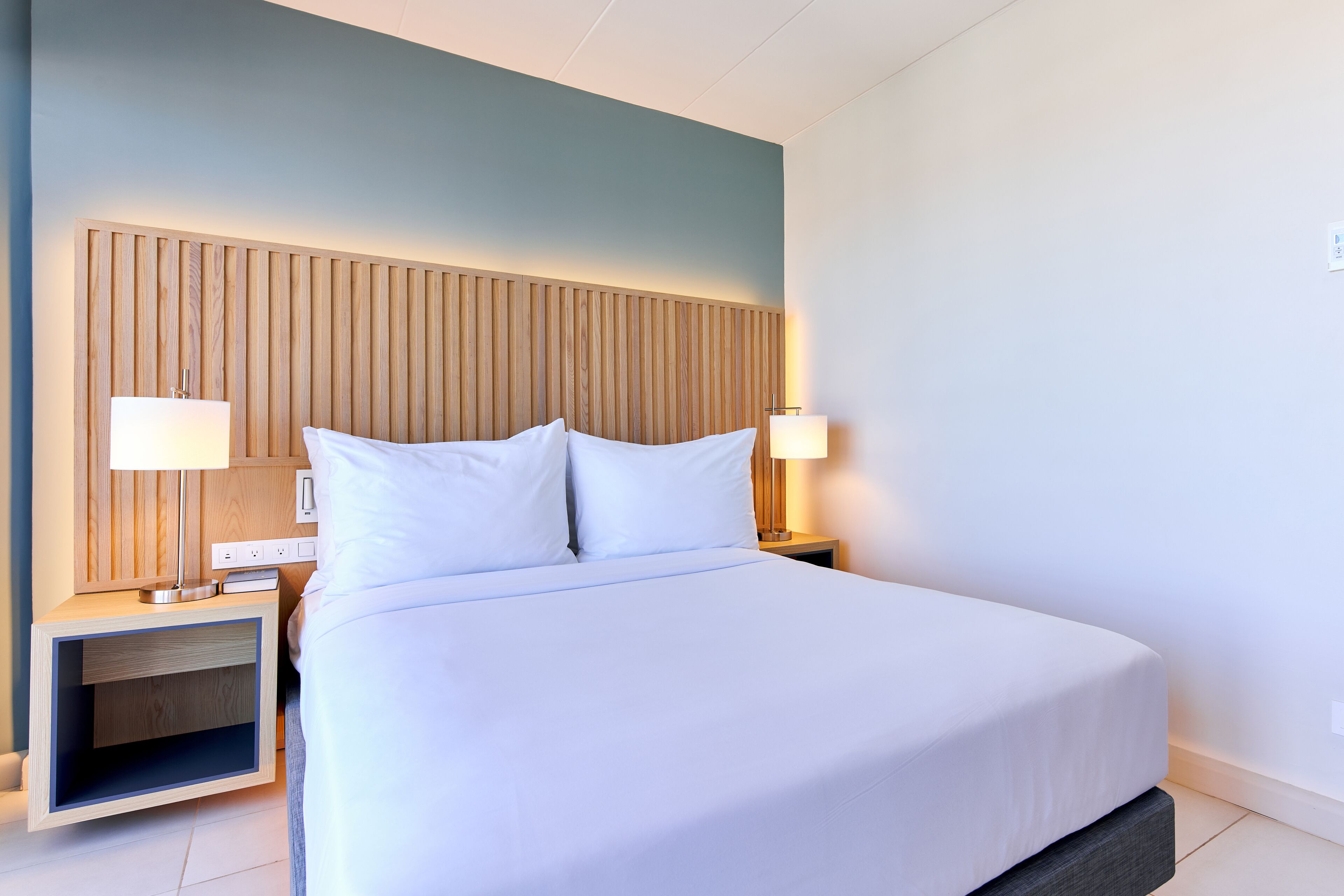 A neatly made bed with white linens, two bedside tables with lamps, and a wooden headboard.