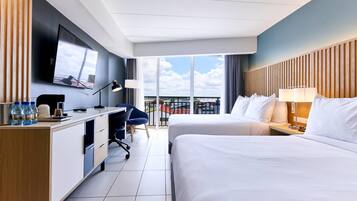 A hotel room with a large bed, a desk, a chair, a TV, and a balcony with a view.