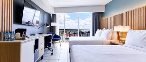 Habitación de hotel con una cama grande, un escritorio con computadora, televisión y balcón con vista a la ciudad.