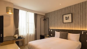 A modern hotel room with a large bed, a desk, a chair, a television, and a wardrobe. - Just Enjoy Business Hotel (Tainan)