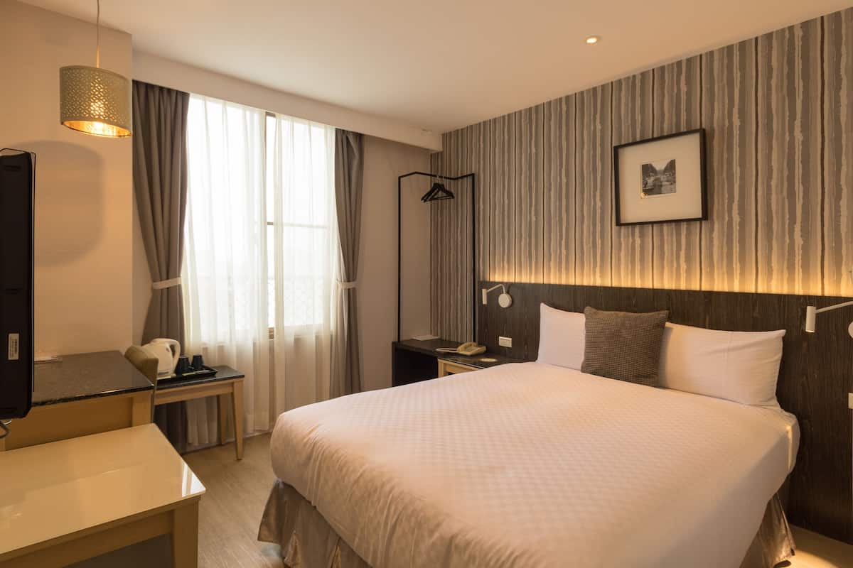 Una habitación de hotel moderna con una cama grande, un escritorio, una silla, un televisor y un armario.