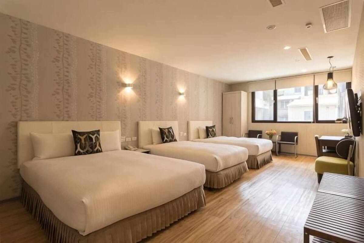 Habitación de hotel con dos camas, un escritorio, una silla y un ventanal grande.