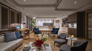 A modern living room with a sofa, armchairs, a coffee table, and a kitchen area in the background. - Just Enjoy Business Hotel (Tainan)