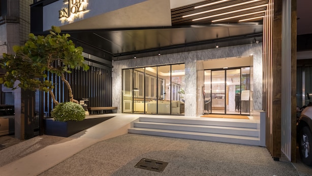A modern hotel entrance with a glass facade, steps leading up to the door, and a small tree in a planter. - Just Enjoy Business Hotel (Tainan)