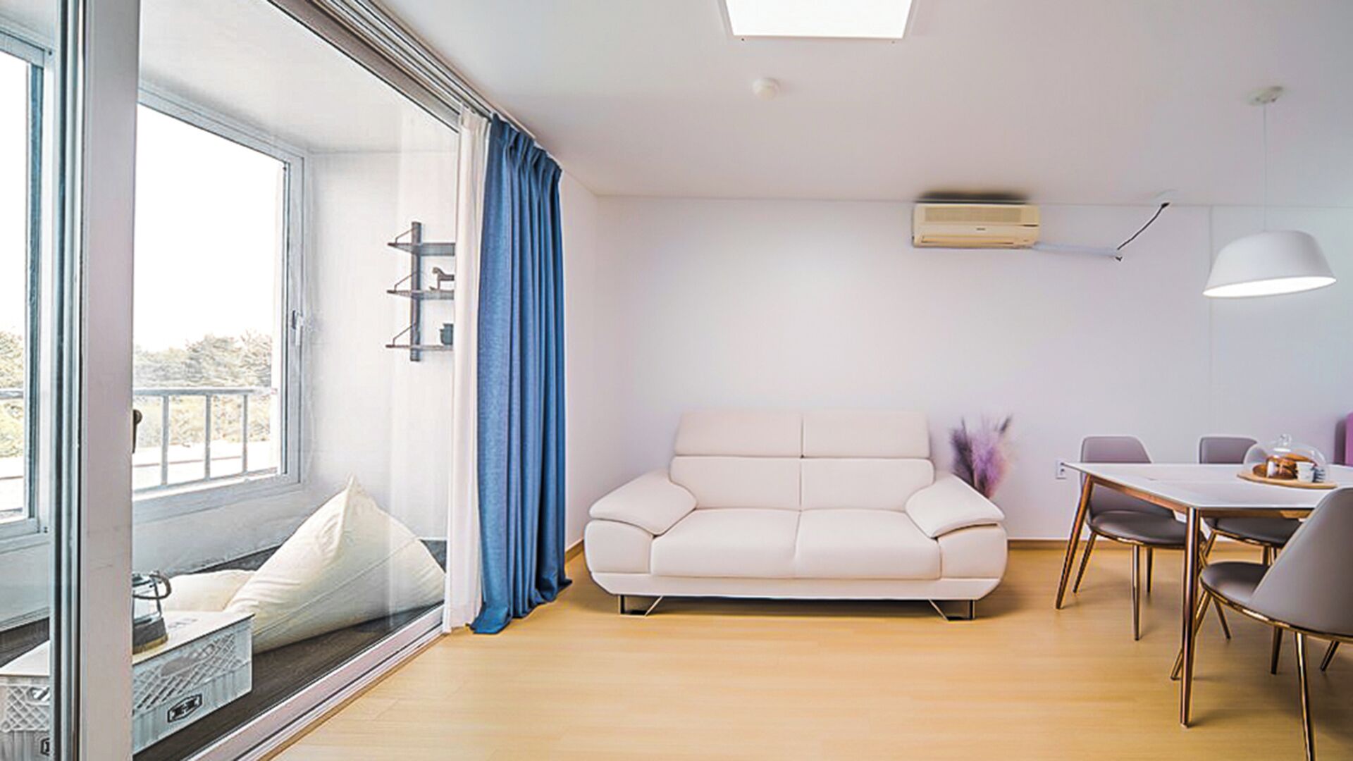 Un salon moderne comprenant un canapé, une table à manger avec des chaises, une grande fenêtre avec des rideaux et un appareil de climatisation.