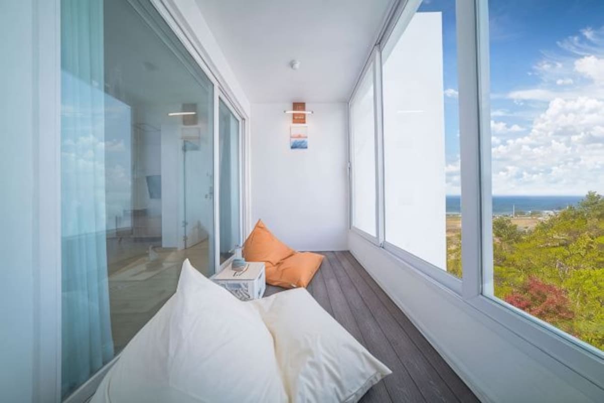 A balcony with a view of the sea, a glass wall, and a wooden floor.