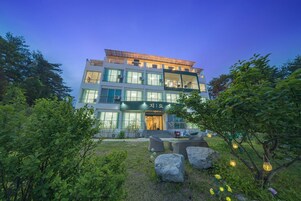 A multi-story hotel with a modern design, featuring large windows and a well-maintained garden with rocks and plants.