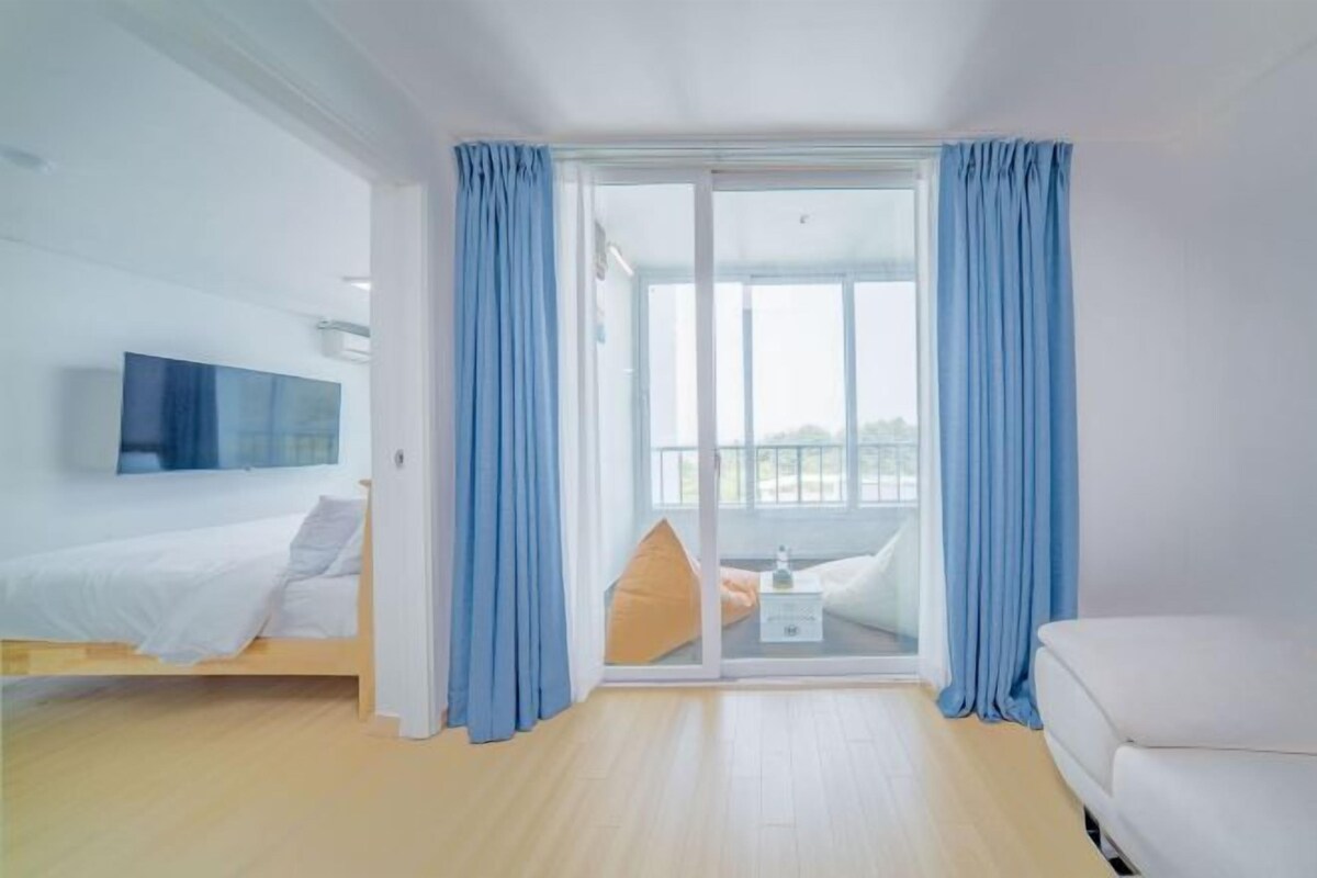 A hotel room with a bed, a sofa, a TV, and a balcony with curtains.