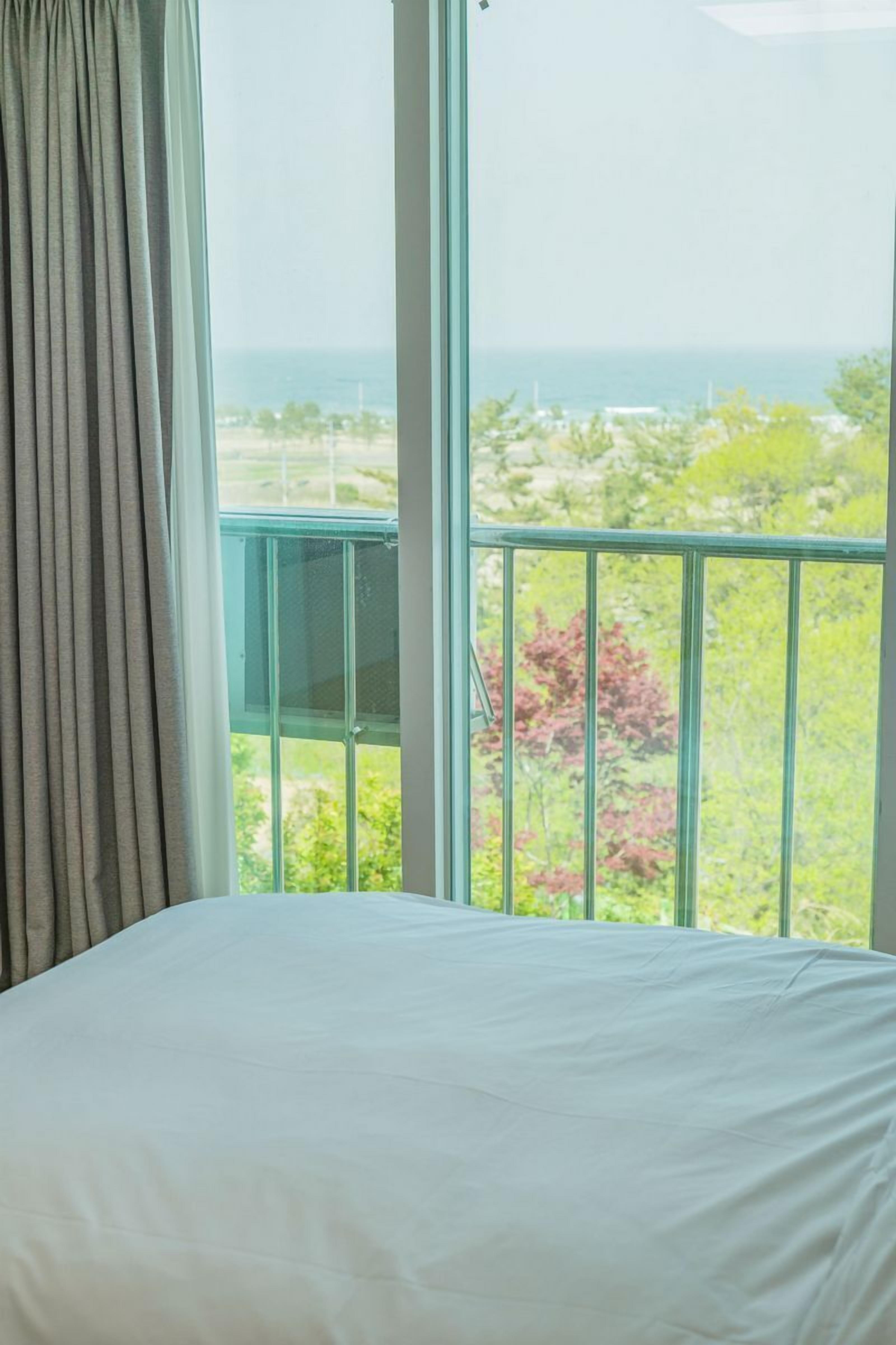 A bedroom with a large window overlooking a scenic view of the sea and greenery.