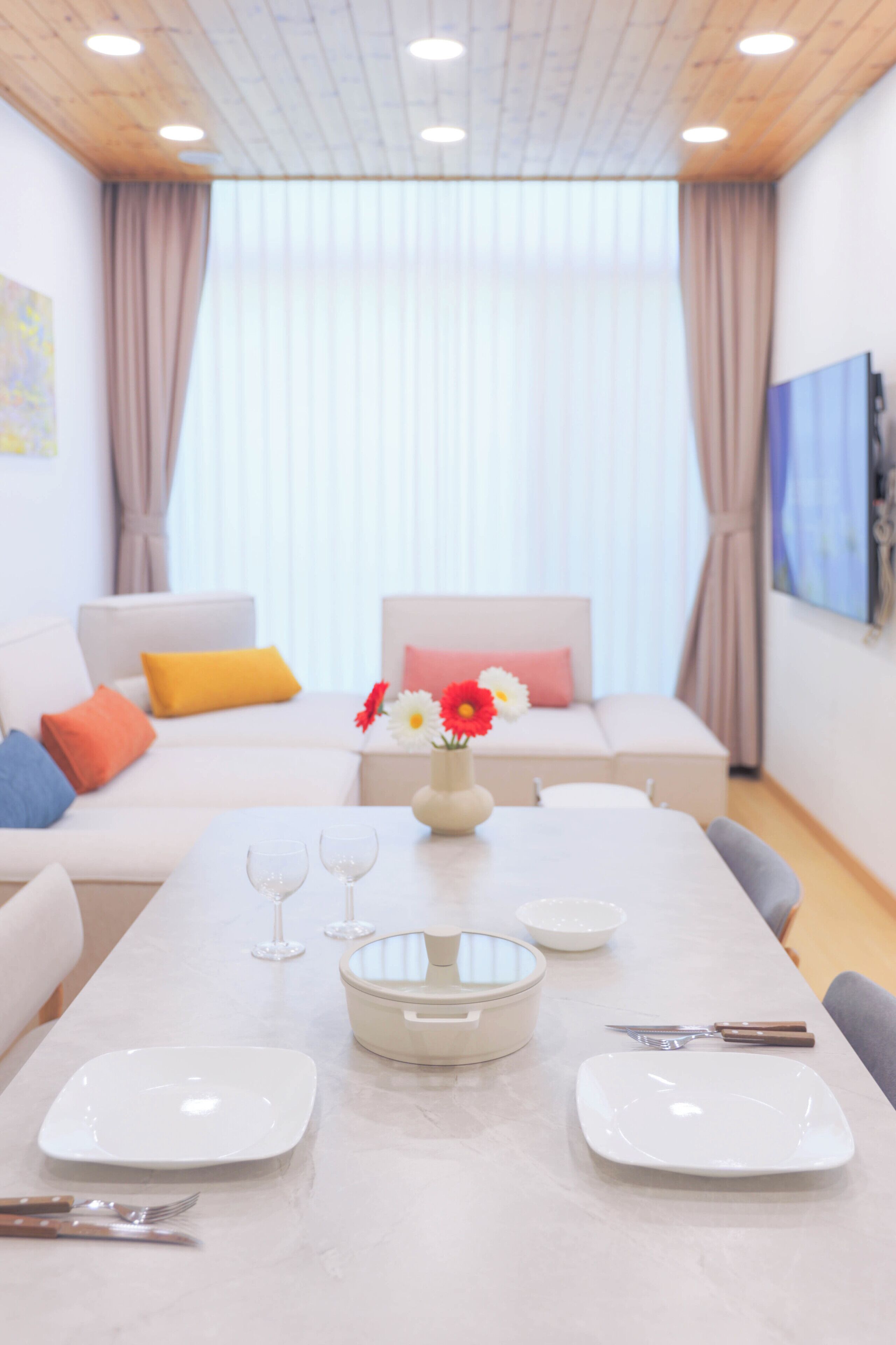 Un salon moderne avec un coin repas, comprenant un ensemble de canapés, une table à manger avec de l’assiette et des couverts blancs, et un vase rempli de fleurs.