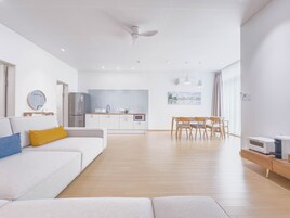 Una sala de estar moderna con un sofá blanco, un comedor con sillas de madera, una cocina con armarios blancos y un ventilador de techo.