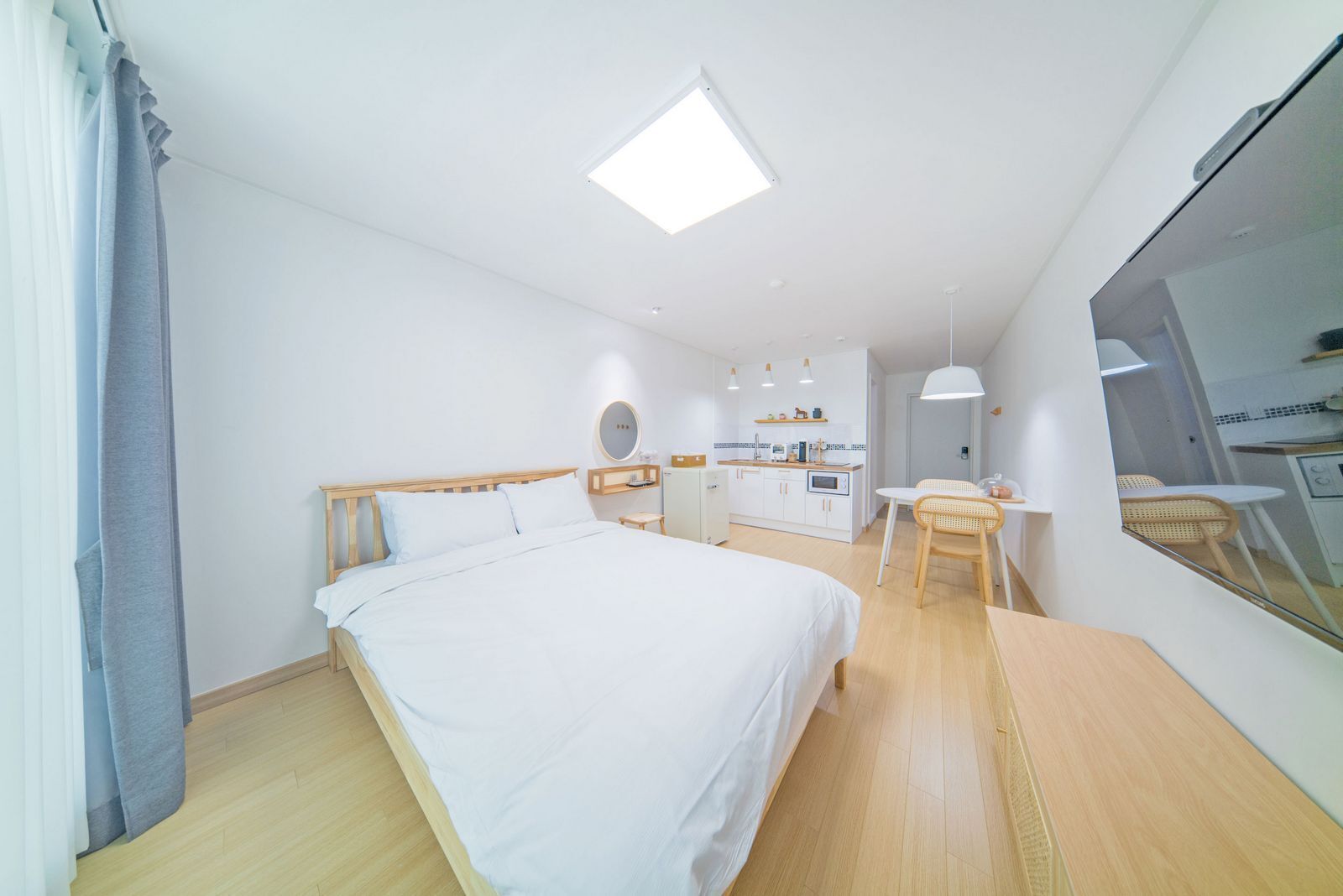 Una habitación de hotel moderna con una cama grande, kitchenette, un área de comedor y un ventanal amplio.