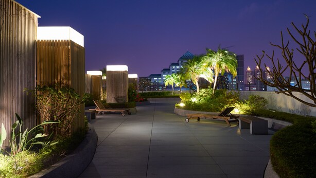 Terraço no telhado com áreas de estar, plantas e um horizonte urbano ao fundo.