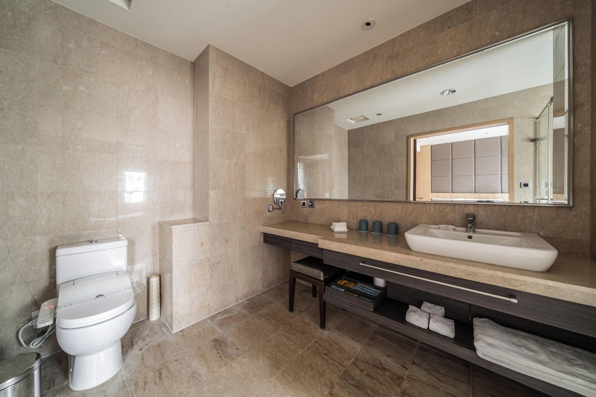 A modern bathroom with a large mirror, a white sink, and a toilet.