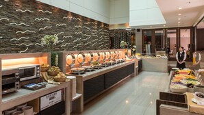Uma área de buffet com diversos pontos de comida, um micro-ondas e uma placa indicando opções de café da manhã.