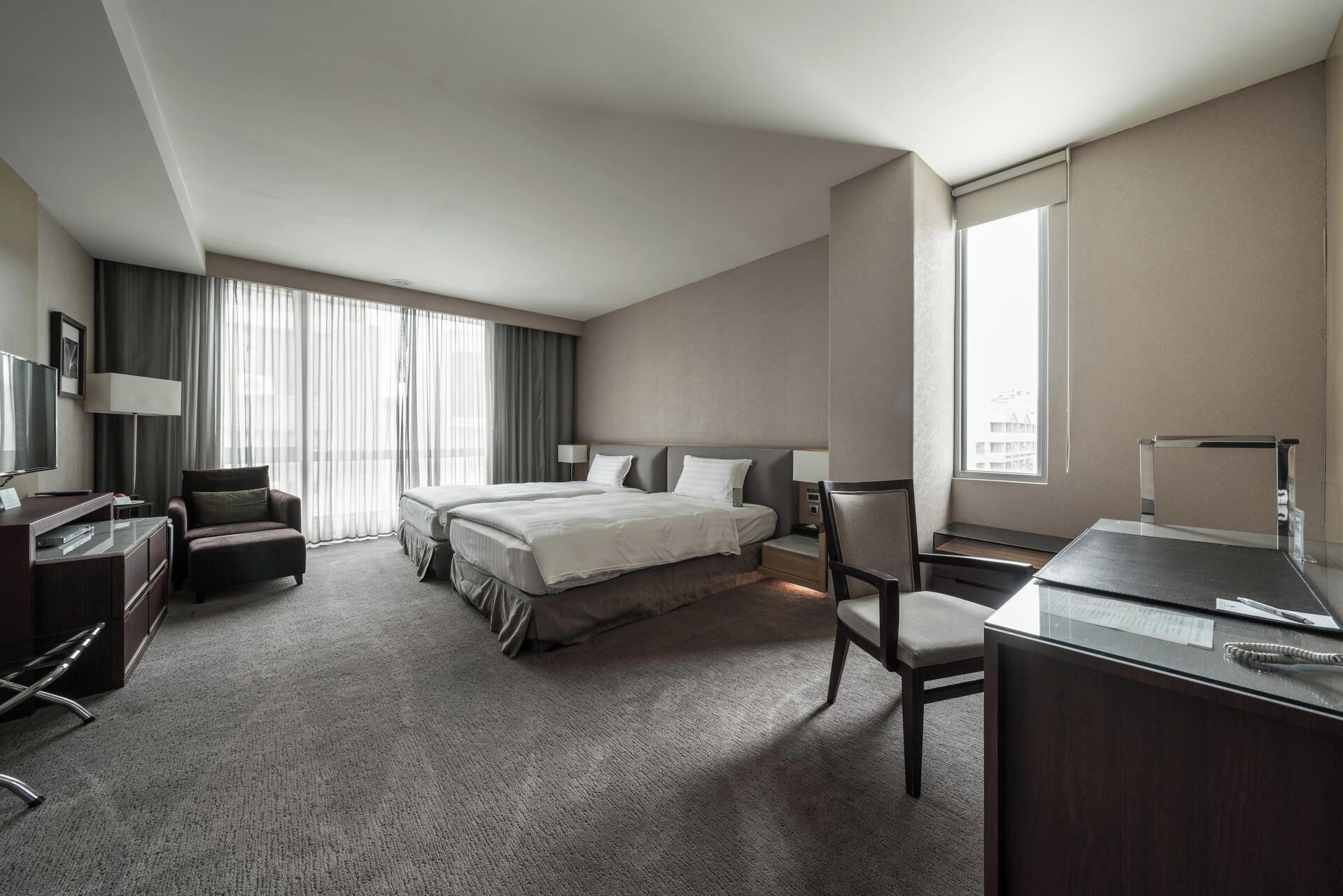 Habitación de hotel con una cama grande, un escritorio, una silla, un televisor y una ventana con cortinas.