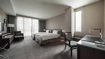 Habitación de hotel con una cama grande, un escritorio, una silla, un televisor y una ventana con cortinas.