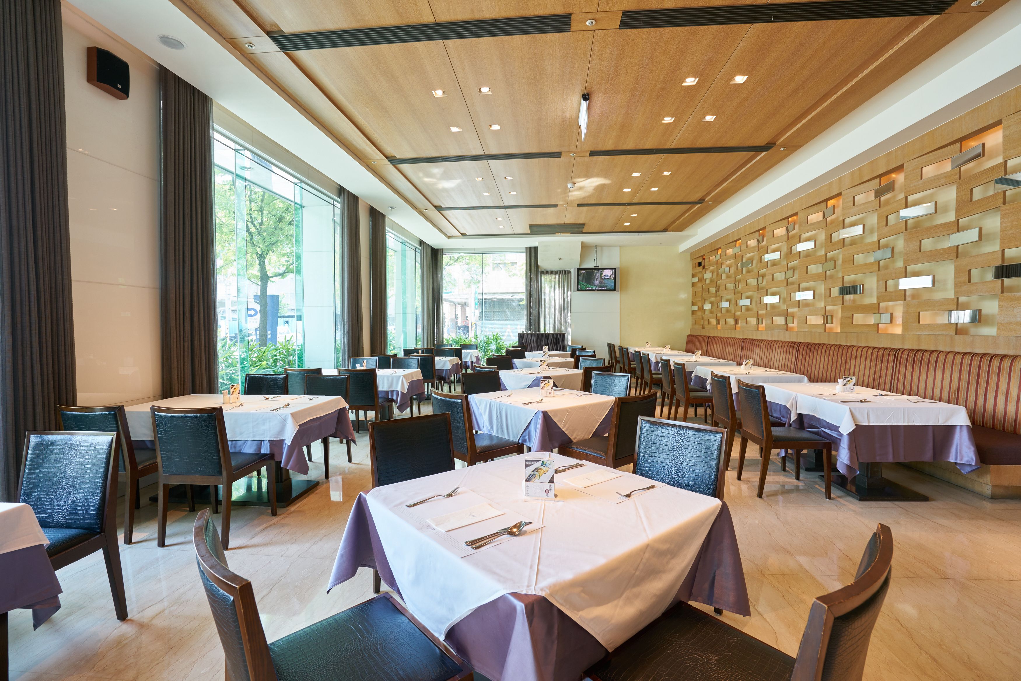 A spacious dining area with multiple tables and chairs, large windows, and a wooden ceiling.