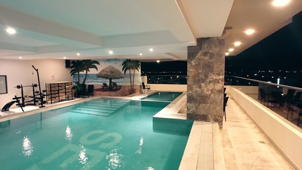 Una piscina con un mural tropical, equipo de ejercicio y vistas de la ciudad de noche.