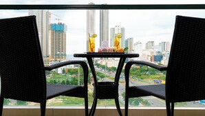 Un balcón con dos sillones de mimbre y una mesita pequeña, con vistas a un paisaje urbano con edificios altos y una carretera.