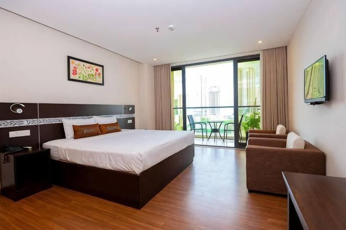 A hotel room with a large bed, a desk, a chair, a TV, and a balcony with a view.