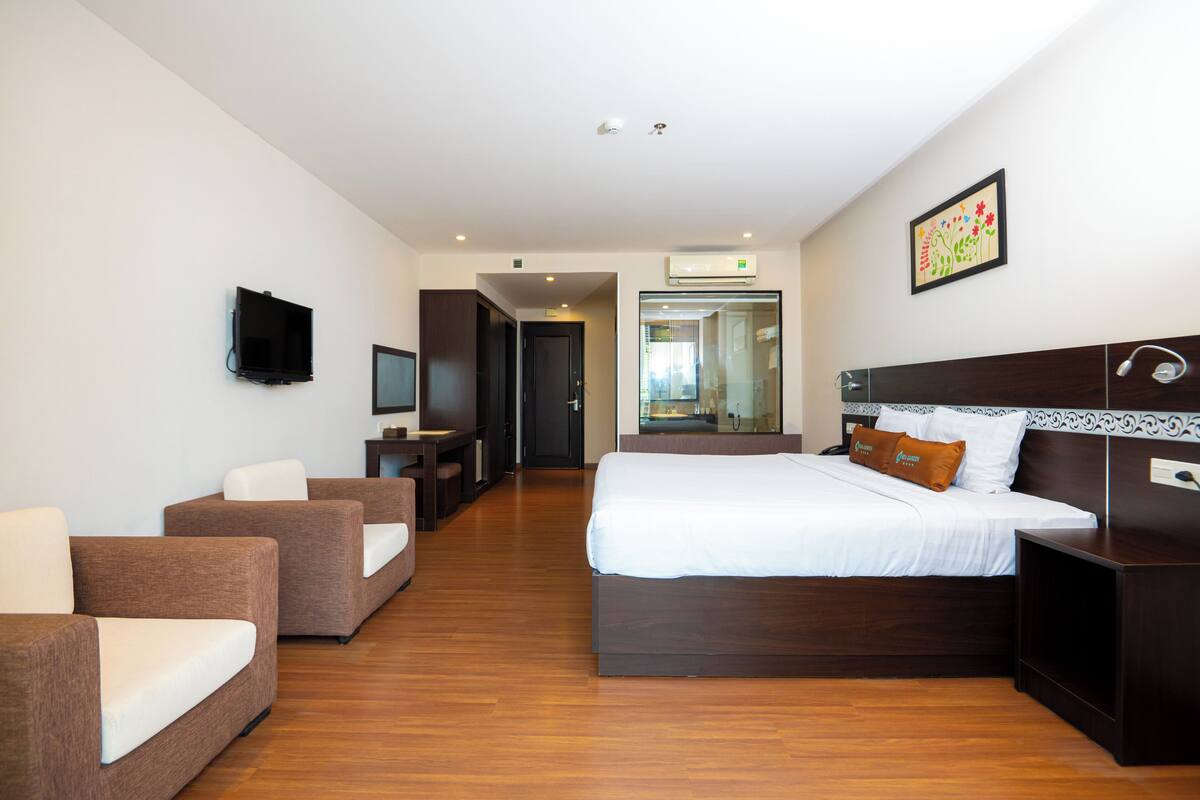 A hotel room with a large bed, two sofas, a TV, and an air conditioning unit.