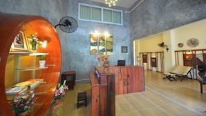 A spacious lobby with a wooden reception desk, a large fan, and a wall-mounted clock. - Phangan Barsay Hostel (Ko Pha-ngan)