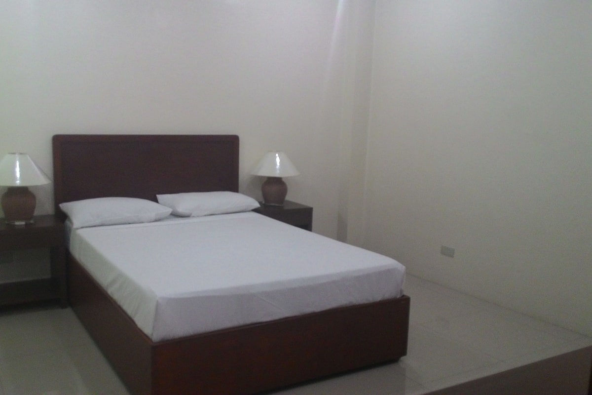 Una cama individual con cabecera de madera, dos mesitas de noche con lámparas y ropa de cama blanca.