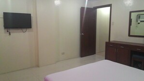 A bedroom with a bed, a TV mounted on the wall, a wardrobe, and a door leading to another room.