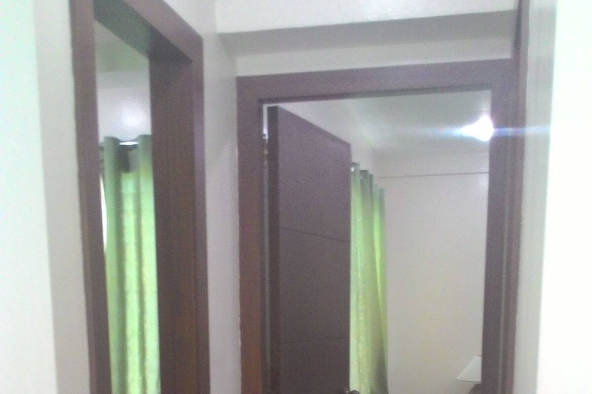 Un pasillo con una puerta de madera, un espejo y una cortina verde.