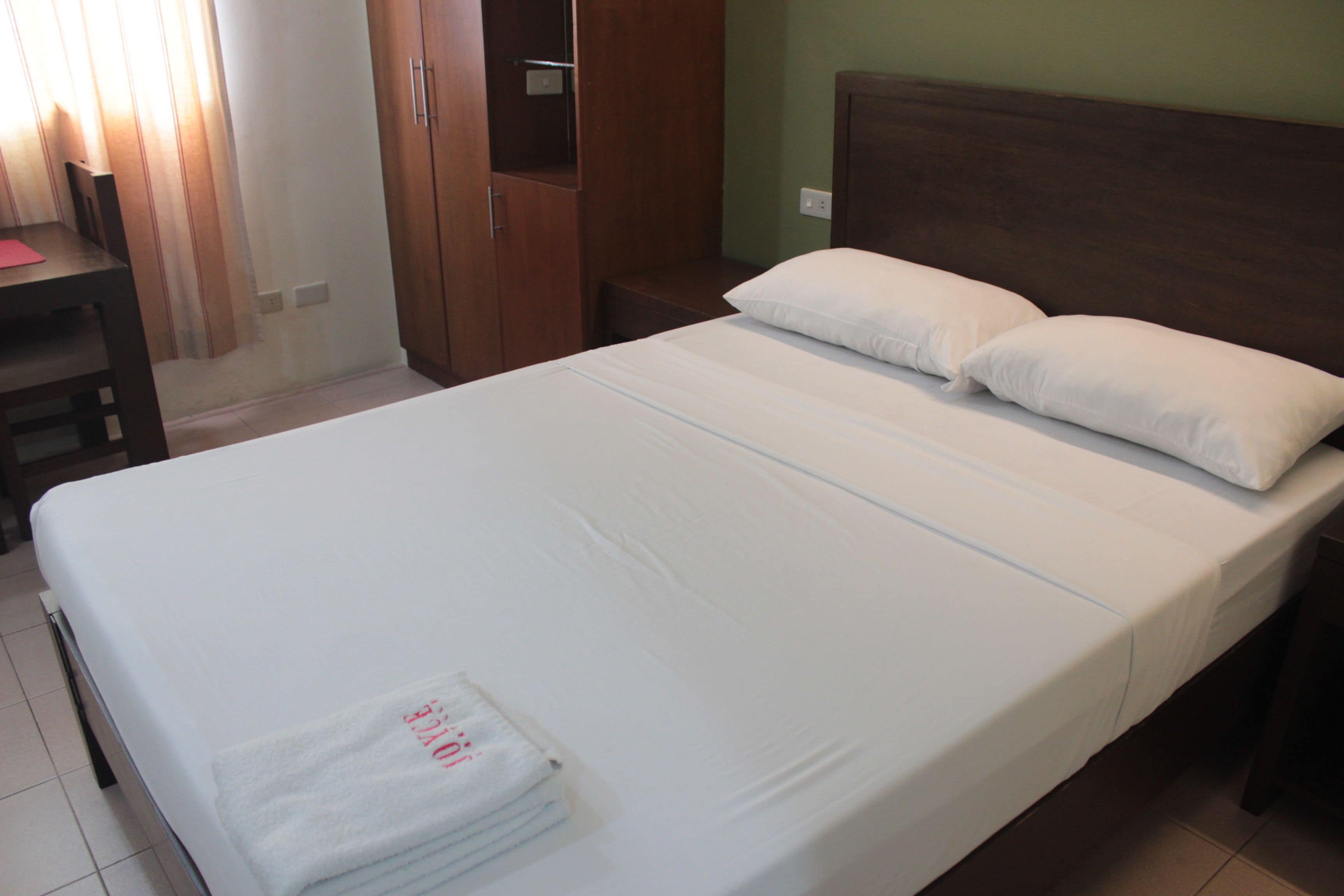A neatly made bed with white linens, a wooden headboard, and a small bedside table.