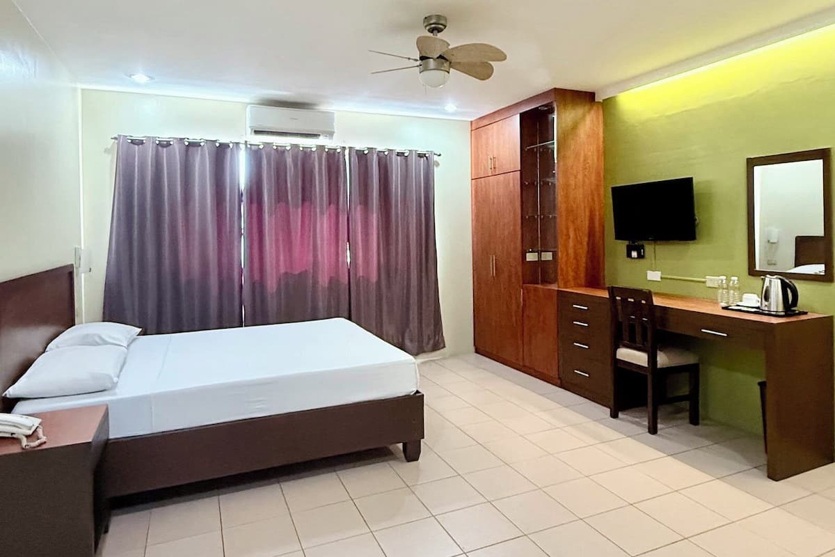 A hotel room with a bed, a desk with a chair, a television, and a wardrobe.