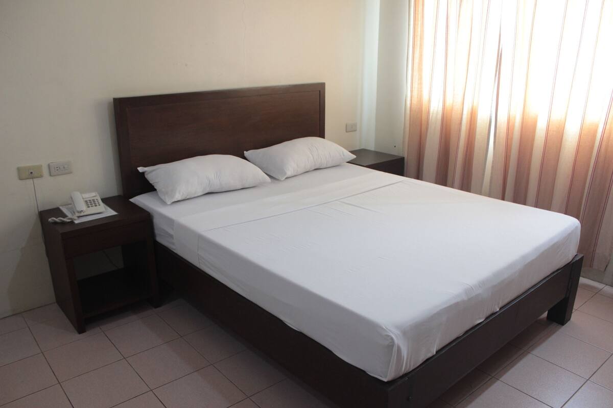 A standard hotel room with a single bed, a nightstand with a telephone, and a window with curtains.