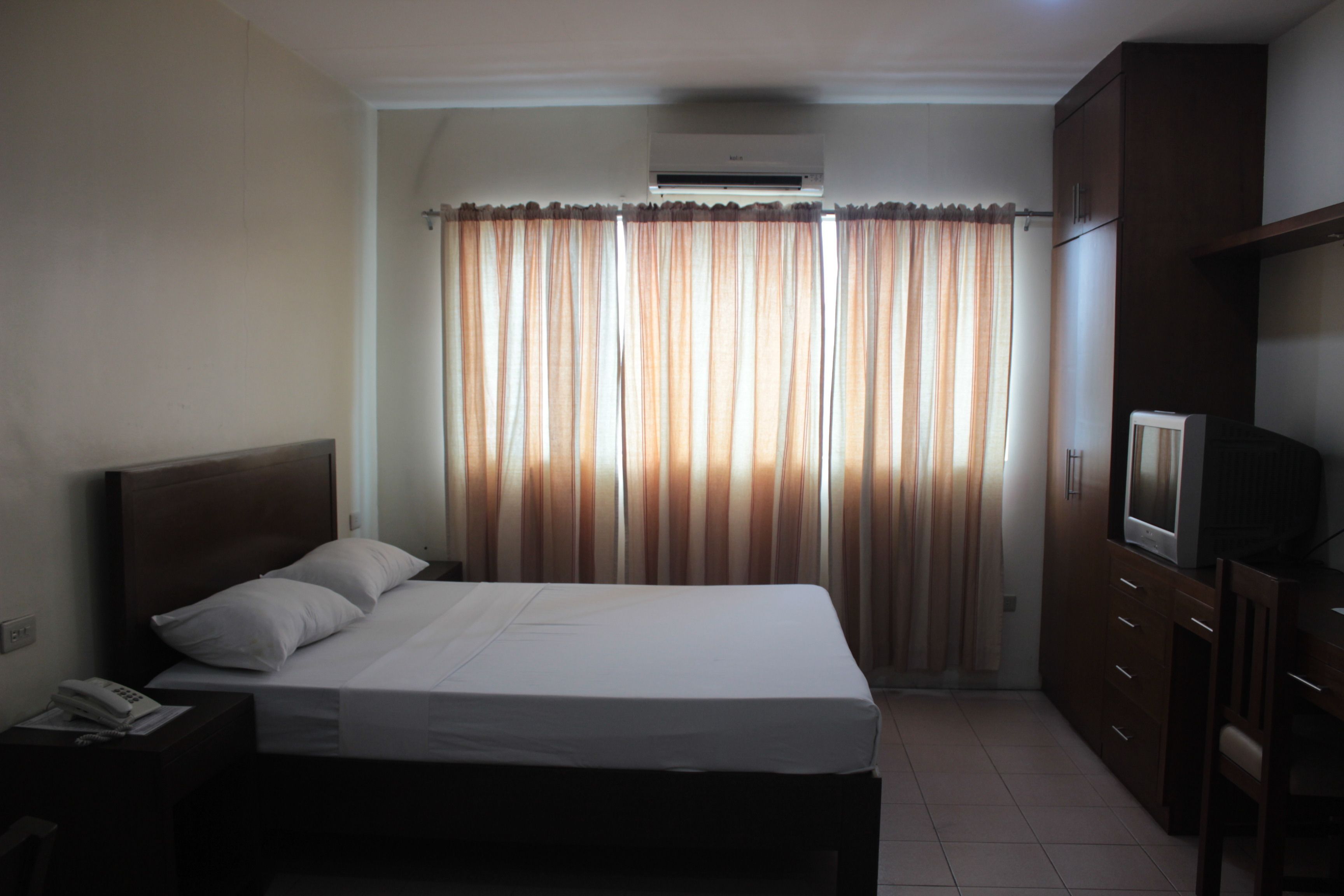 A hotel room with a bed, a TV, a wardrobe, and an air conditioning unit.